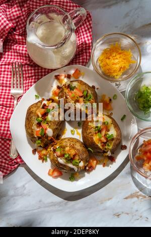 Pommes de terre cuites au four avec fromage cheddar, morceaux de bacon émiettés, échalotes tomates en dés et sauce ranch Banque D'Images