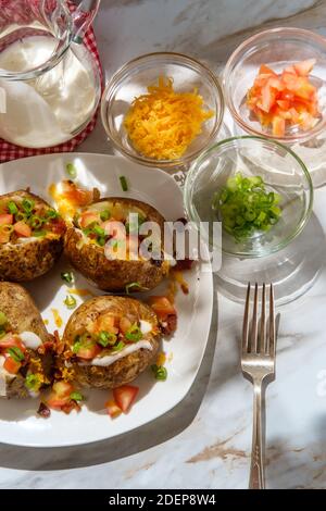 Pommes de terre cuites au four avec fromage cheddar, morceaux de bacon émiettés, échalotes tomates en dés et sauce ranch Banque D'Images