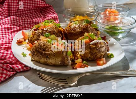 Pommes de terre cuites au four avec fromage cheddar, morceaux de bacon émiettés, échalotes tomates en dés et sauce ranch Banque D'Images