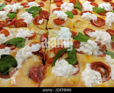 Gros plan de pizza italienne traditionnelle par tranche (Pizza al Taglio) avec tomates cerises, fromage mozzarella de buffle frais, feuilles de basilic et extra virg Banque D'Images