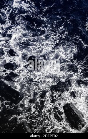 Eau et rochers (duotone) . De petites vagues s'écrasont sur un rivage rocheux et créent des tourbillons de mousse blanche, vus d'en haut Banque D'Images