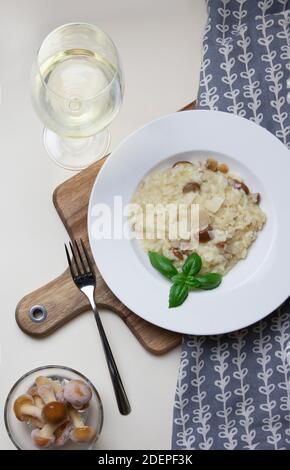 Risotto végétarien gastronomique aux champignons sur une plaque blanche, fond jaune, servi avec un verre de vin blanc. Un plat de riz du nord de l'Italie cuit avec du bouillon jusqu'à ce qu'il atteigne une consistance crémeuse. Banque D'Images