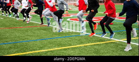 Une équipe de garçons et de filles d'école secondaire effectuant des exercices de course actifs sur un terrain de gazon vert à l'extérieur dans le froid de l'hiver. Banque D'Images