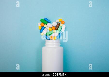 Comprimés multicolores et capsules en forme de cœur, flacon blanc pour comprimés, pilules pharmaceutiques sur fond bleu, analgésique contre la maladie Banque D'Images