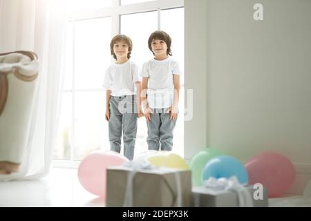 Deux adorables garçons latins jumeaux, petits enfants en vêtements décontractés, heureux, saluant leurs parents, préparant des ballons colorés et des boîtes-cadeaux pour eux. Vacances, cadeaux, concept d'enfance Banque D'Images