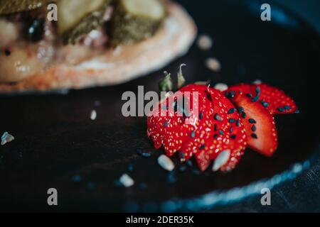 Gros plan de fraises tranchées sur une pierre noire assiette avec un sandwich sur le côté Banque D'Images