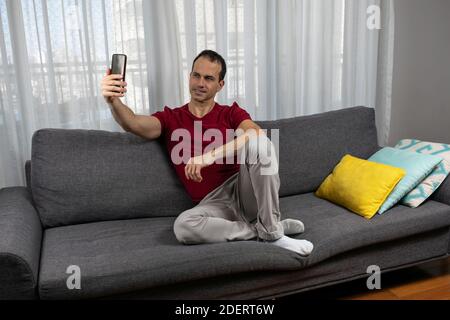 Homme mature (44 ans) assis sur le canapé, portant des chaussettes et prenant une photo de lui-même. Banque D'Images
