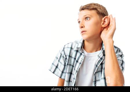 Le garçon entend, met sa main à l'oreille pour mieux entendre, dans le Studio sur fond blanc Banque D'Images