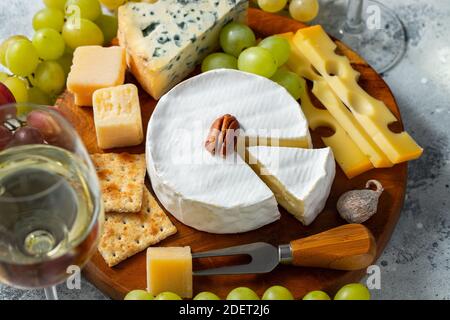 Dégustation de fromages sur une assiette en bois. Nourriture pour le vin et la date romantique, fromage delicatessen sur un fond de béton léger Banque D'Images