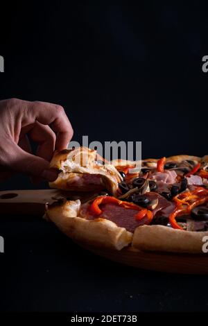 Un gros plan d'une personne prenant une tranche d'un une délicieuse pizza fraîchement cuite sur un plateau en bois Banque D'Images