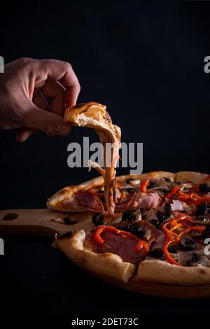 Un gros plan d'une personne prenant une tranche d'un une délicieuse pizza fraîchement cuite sur un plateau en bois Banque D'Images