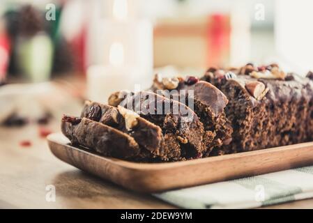 Délicieux gâteau de fruits de Noël aux noix séchées sur une assiette en bois avec des éléments décoratifs flous en arrière-plan Banque D'Images