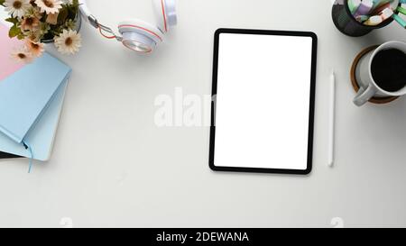 Photo à plat de l'espace de travail indépendant avec tablette à écran vide, carnet, tasse à café et casque sur table blanche. Banque D'Images