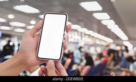 Prise de vue courte des mains d'un homme tenant un téléphone portable avec écran blanc sur fond noir du terminal de l'aéroport. Banque D'Images