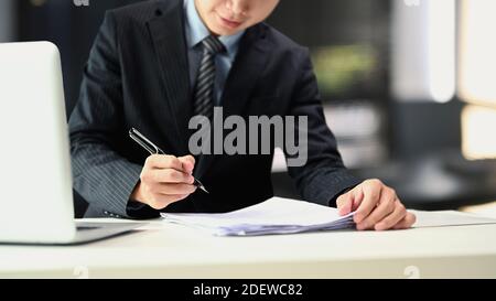 Un homme d'affaires en costume noir tient des stylos signer dans les documents sur la table au bureau. Banque D'Images