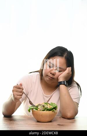 Portrait de la femme en surpoids est fatigué des restrictions de régime alimentaire manger de la salade verte assis à la table. Banque D'Images