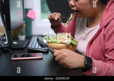 Une jeune femme en surpoids s'est assise à table et a mangé de la salade saine à son espace de travail. Banque D'Images