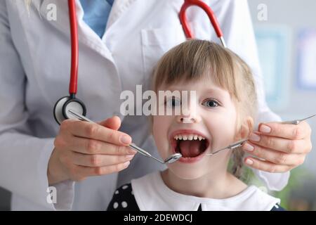 Dentiste médecin avec stéthoscope examine les dents de la petite fille dedans clinique Banque D'Images