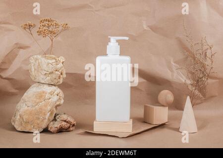 Crème, lotion hydratante, shampooing ou autre produit cosmétique en bouteille blanche sur pierre, formes géométriques en bois et fleurs séchées sur papier beige Banque D'Images