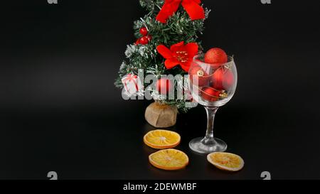 Arbre du nouvel an sur fond noir. Boules de Noël rouges dans un verre à vin, décor d'oranges sèches Banque D'Images