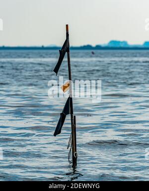 Poteau avec des drapeaux marquant l'emplacement des filets de pêche sous-marins le long du rivage. Banque D'Images