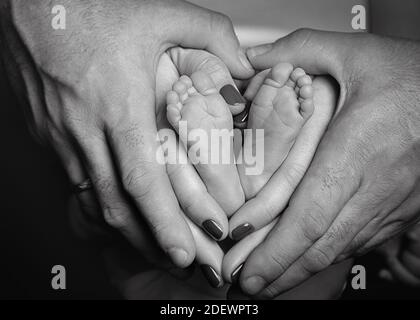 l'image en noir et blanc du nouveau-né, du père et de la mère tient les pieds du bébé forme un coeur Banque D'Images