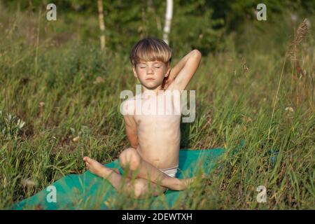 Portrait d'enfant de garçon pratiquant le yoga, assis dans ggomukhasana exercice, posture de vache en train de faire de l'exercice à l'extérieur dans le parc Banque D'Images