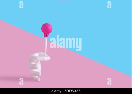 Une main en plastique tenant une lollipop sur un rose et arrière-plan bleu Banque D'Images