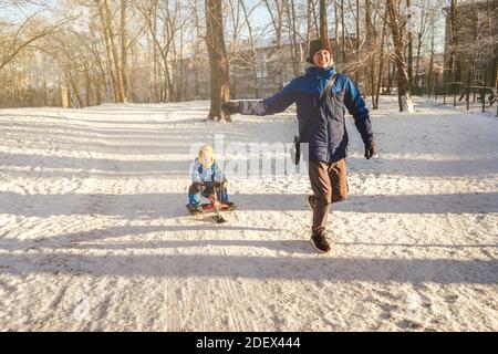 Un homme court et roule un petit garçon sur une motoneige à travers la neige de la montagne dans le parc. Banque D'Images