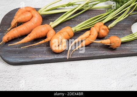 Les racines de carottes laides se trouvent sur une planche à découper en bois sur un fond clair. Banque D'Images