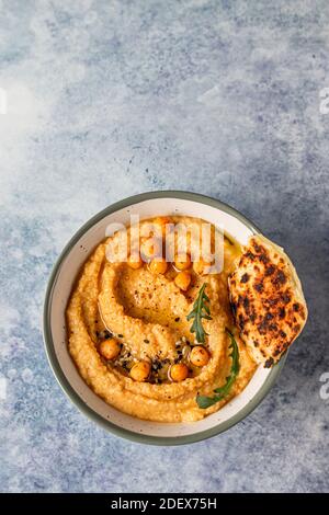 Bol avec houmous faits maison garni de pois chiches bouillis, graines, pain plat et huile d'olive, fond en béton bleu. Mise au point sélective. Vue de dessus. Banque D'Images