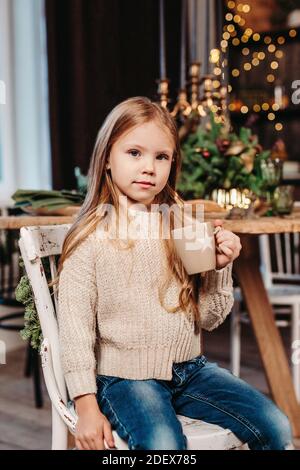 Petite fille buvant du cacao à la maison contre fond de Noël Banque D'Images