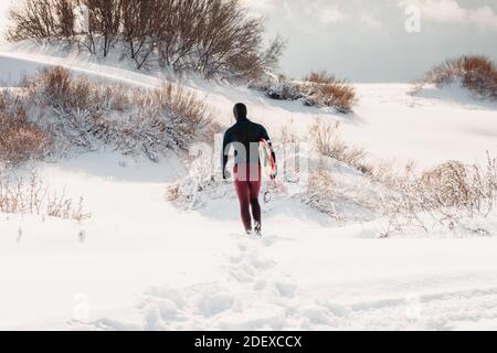 Hiver enneigé et homme surfant avec planche de surf. Côte d'hiver et surf en combinaison. Banque D'Images