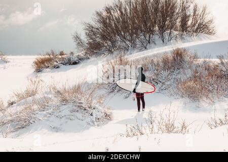 Hiver enneigé et homme surfant avec planche de surf. Côte d'hiver et surf en combinaison. Banque D'Images