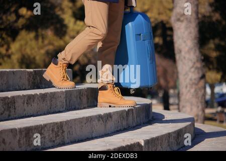 Gros plan d'un jeune homme méconnaissable descendant des escaliers dans la rue avec sa valise dans la main, fatigué après un long voyage. Voyage d'affaires 2021. Banque D'Images