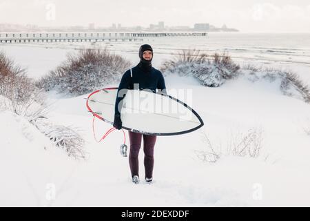 Hiver enneigé et homme surfant avec planche de surf. Côte d'hiver et surf en combinaison. Banque D'Images