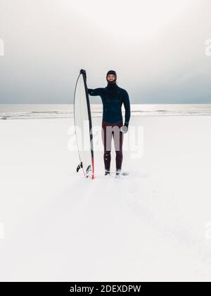 Hiver enneigé et homme surfant avec planche de surf. Côte d'hiver et surf en combinaison. Banque D'Images