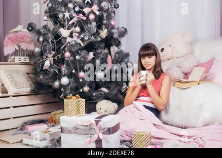 Une fille boit un verre d'une tasse assise dans le salon de Noël rose, sur fond d'un arbre de Noël. Photo de haute qualité Banque D'Images