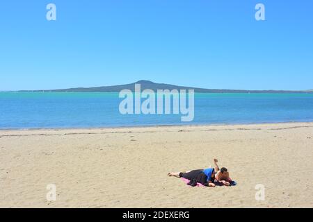 AUCKLAND, NOUVELLE-ZÉLANDE - 28 novembre 2020 : vue de couple sur la plage de St Heliers Bay avec l'île Rangitoto en arrière-plan Banque D'Images