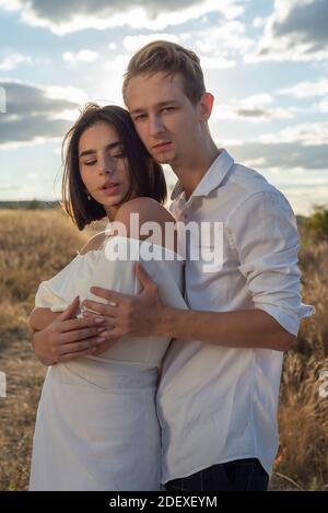 portrait d'un jeune homme et d'une fille de vingt-deux ans. Mariage de la génération Z. Sur la toile de fond d'un ciel nuageux, un soleil couchant dans un champ. Banque D'Images