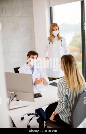 Couple médical médecins avec masques médicaux de protection du visage parler avec jeune femme et l'utilisation de l'ordinateur dans l'offic Banque D'Images