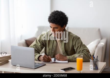 Concept de homeschooling. Étudiant noir écrivant en copybook pendant la conférence en ligne ou la leçon web à la maison Banque D'Images