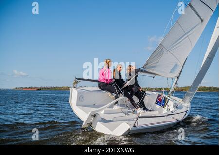 Un beau yacht blanc navigue dans le vent sur la rivière sur le fond d'une belle forêt d'automne. Un gars à bord avec deux filles Banque D'Images