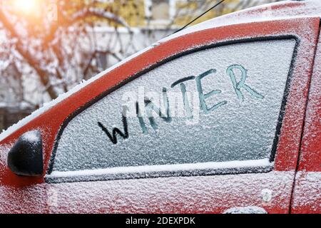 Mot Winter écrit avec le doigt sur une fenêtre latérale enneigée d'une voiture Banque D'Images