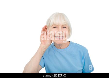 Concept de surdité. Femme âgée souriante avec une main sur l'oreille écoutant des sons et des voix, isolée sur blanc Banque D'Images