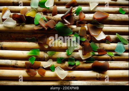 Broken, montées des morceaux de verre colorés polis par l'eau de mer sur le parquet de bambou. Banque D'Images