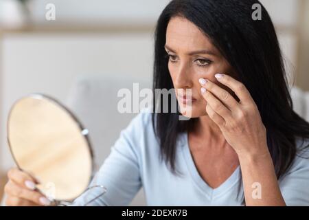 Femme adulte vérifiant son visage dans le miroir, touchant le visage Banque D'Images