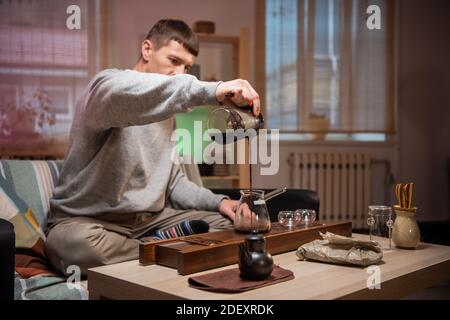 Préparation d'un délicieux thé chinois fort. Scène d'une véritable cérémonie de thé oriental à la maison avec un ensemble spécial d'outils en bambou. Le maître de thé verse de l'eau chaude dans un bol Banque D'Images