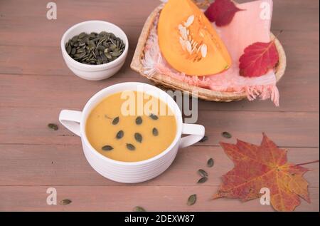 Sur fond de bois, une assiette avec soupe de purée de citrouille, un morceau de citrouille, graines de citrouille et feuilles d'automne. Banque D'Images