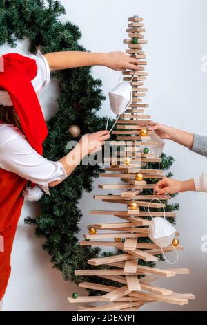 Une jeune femelle dans un chapeau nain rouge décorera un arbre de Noël stylisé avec des masques de visage, coronavirus et concept de Noël Banque D'Images